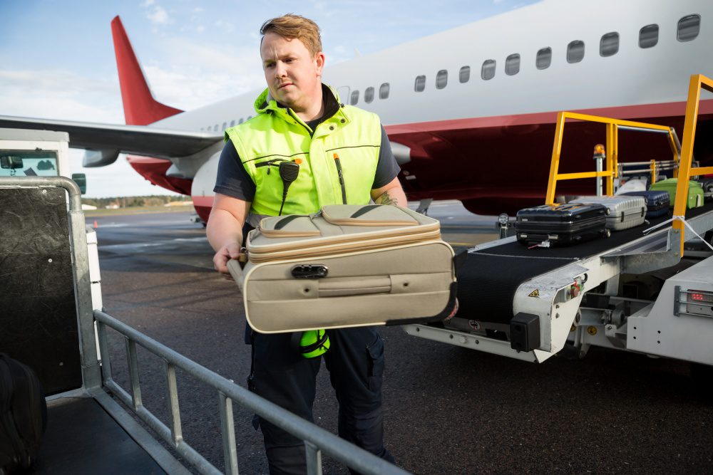 Airport-employee-loading-luggage-on-plane (1) Airport employee removing luggage from plane
